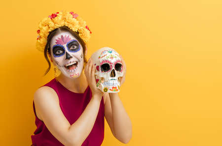 Adorable zombie in flower wreath posing on yellow background. Happy woman with Halloween creative...