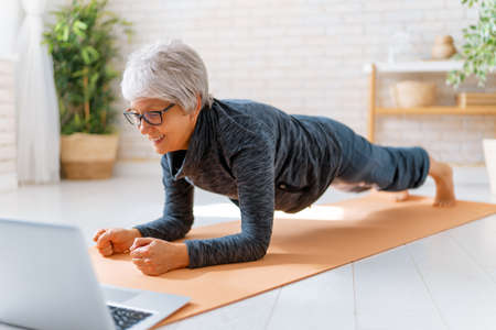 Senior woman in activewear watching online courses on laptop while exercising at home.の写真素材