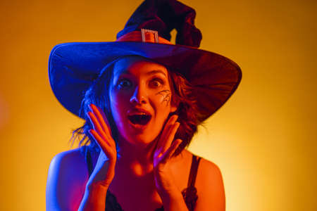 Happy Halloween! Young woman in black witch costume on party in color lighting.の写真素材