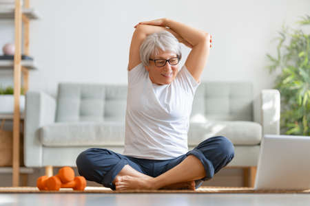 Senior woman in activewear watching online courses on laptop while exercising at home.の写真素材