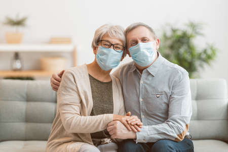 Senior couple wearing facemasks during coronavirus and flu outbreak. Virus and illness protection, home quarantine. COVID-2019. Taking on or taking off masks.の写真素材
