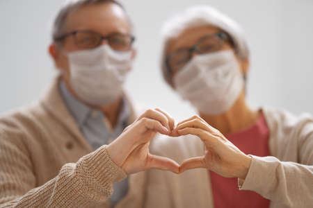 Senior couple wearing facemasks during coronavirus and flu outbreak. Virus and illness protection, home quarantine. COVID-2019. Taking on or taking off masks.の写真素材