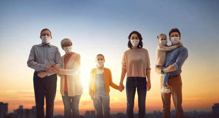 Family is wearing facemasks during coronavirus and flu outbreak. Virus and illness protection, quarantine. COVID-2019. People on sunset city landscape background.の写真素材