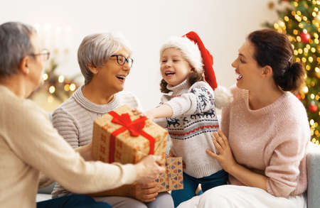 Merry Christmas and Happy Holidays! Grandma, grandpa, mum and child exchanging gifts. Parents and...