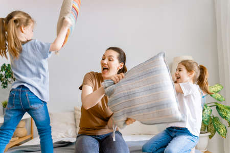 Happy loving family! The mother and her children girls are fighting pillows on bed at home.の写真素材