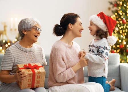 Merry Christmas and Happy Holidays! Cheerful kid presenting gifts to mom and granny. Parents and...