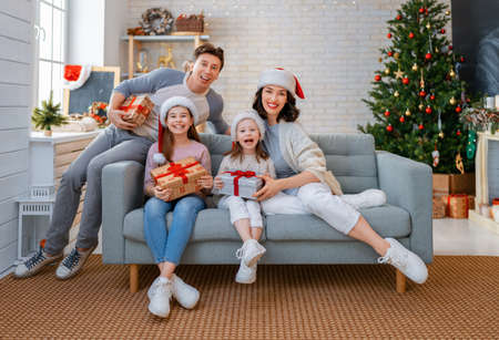 Merry Christmas! Pretty young mother, father and daughters with presents near Christmas tree.
