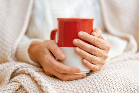 Senior woman with a mug in hands close up. Winter warming up concept.