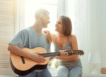 Happy couple in love. Stunning sensual portrait of young stylish fashion couple indoors. Young man playing guitar for his beloved girl.の写真素材