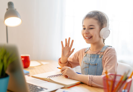 Back to school. Happy child is sitting at desk. Girl doing homework or online education.の写真素材