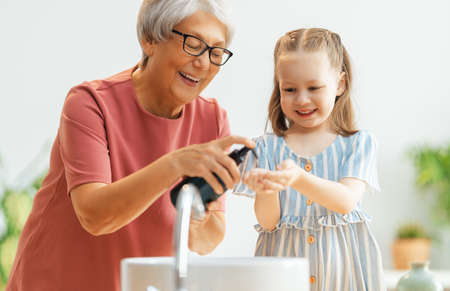 A cute little girl and her grandmother are washing their hands. Protection against infections and viruses.の写真素材