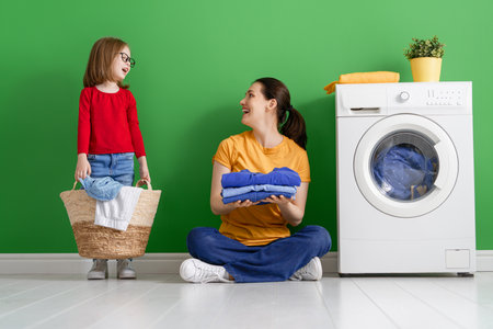 Beautiful young woman and child girl little helper are having fun and smiling while doing laundry at home.の写真素材