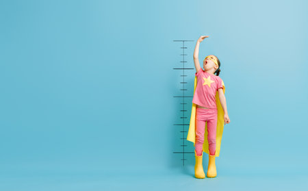 Little child is playing superhero. Kid is measuring the growth on the background of color wall. Girl power concept.の写真素材