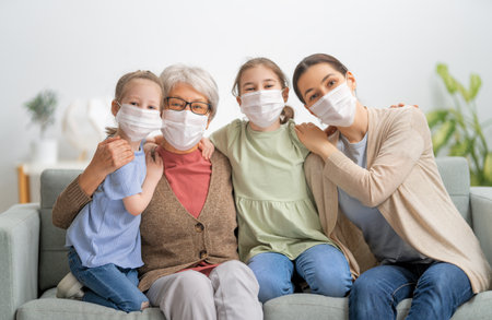 A nice girls, her mother and grandmother enjoying spending time together at home. People wearing face masks.の写真素材