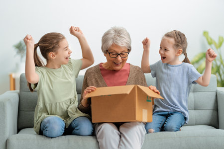 Grandmother and granddaughters are unpacking cardboard box at home.の写真素材