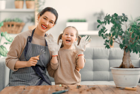 Cute child girl helping her mother to care for plants. Mom and her daughter engaging in gardening at home. Happy family in spring day.の写真素材