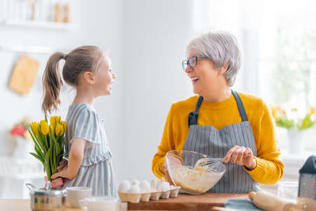 Happy loving family are preparing bakery together. Little girl is giving flowers to her granny in...