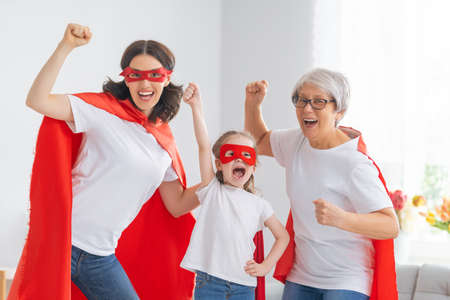 Grandmother, mother and child playing together. Girl and women in Superhero costumes. Family holiday and togetherness.の写真素材