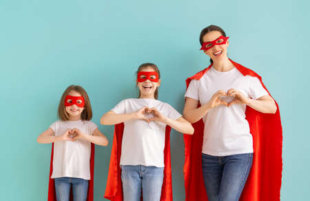 Mother and her children playing together. Girls and mom in Superhero costumes having fun and...