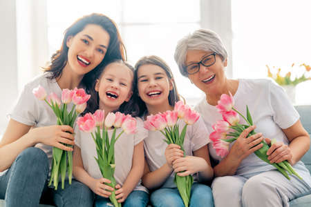 Happy women's day! Child daughters are congratulating mom and granny giving them flowers tulips. Grandma, mum and girls smiling and hugging. Family holiday and togetherness.の写真素材