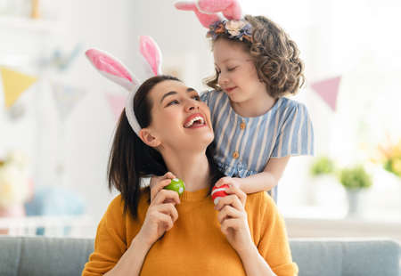 Happy holiday! Mother and her daughter with painting eggs. Family celebrating Easter. Cute little...