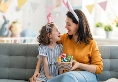 Happy holiday! Mother and her daughter with painting eggs. Family celebrating Easter. Cute little child girl is wearing bunny ears.の写真素材