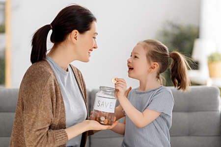 Mother and daughter are holding moneybox, girl putting coin.  moneybox, girl putting coin.の写真素材