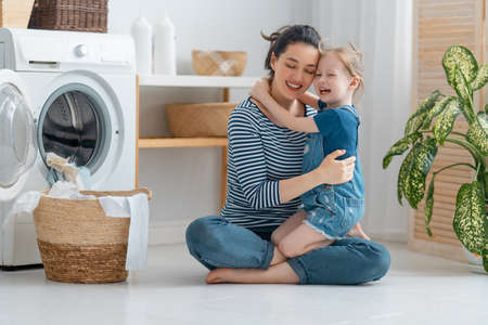 Beautiful young woman and child girl little helper are having fun and smiling while doing laundry at home.の写真素材