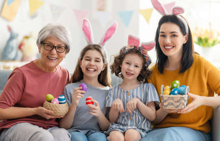 Happy holiday! Mother and her daughters with painting eggs. Family celebrating Easter. Cute little children girls are wearing bunny ears.の写真素材