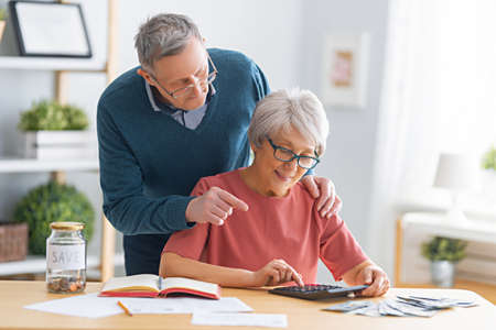 Elderly married couple sitting at the desk with a paper receipt in hands are calculating expenses, managing the family budget.の写真素材