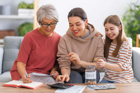 Two women and child, sitting on the sofa with a paper receipt, are calculating expenses, managing the family budget.の写真素材