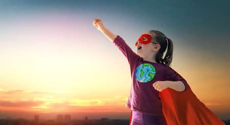 Earth day concept. Child superhero with symbol of ecological worldviews on sunset cityscape background.の写真素材