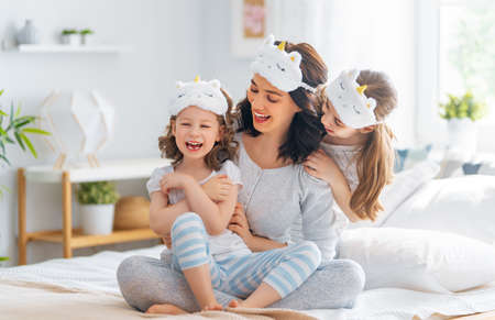 Nice girls and their mother enjoying sunny morning. Good time at home. Children waking up from sleep. Family playing on the bed in the bedroom.の写真素材