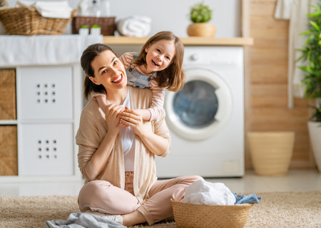 Beautiful young woman and child girl little helper are having fun and smiling while doing laundry at home.の写真素材