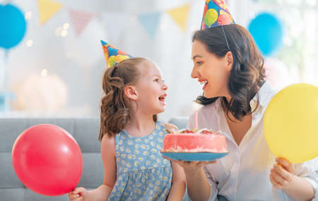 The kid is blowing out the candles on the cake. Mother and daughter are celebrating birthday.