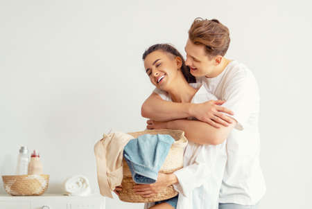 Beautiful young loving couple is smiling while doing laundry at home.の写真素材