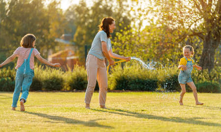 Happy family playing in backyard. Mother sprinkling her kids in hot summer day.の写真素材