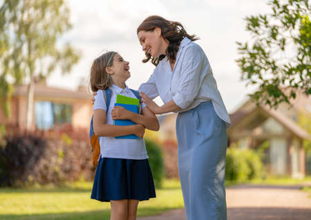 Parent and pupil of primary school going hand in hand. Woman and girl with backpack behind the back. Beginning of lessons.の写真素材