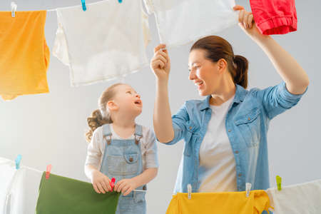 Beautiful young woman and child girl little helper are having fun and smiling while doing laundry and drying.の写真素材