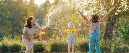 Happy family playing in backyard. Mother sprinkling her kids in hot summer day.の写真素材