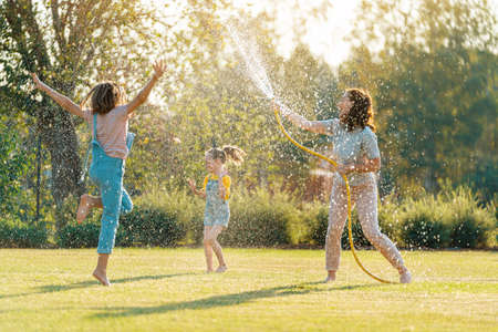 Happy family playing in backyard. Mother sprinkling her kids in hot summer day.の写真素材