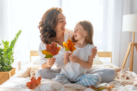A nice girl and her mother enjoying sunny morning. Good time at home. Child wakes up from sleep. Family playing on the bed in the bedroom.の写真素材
