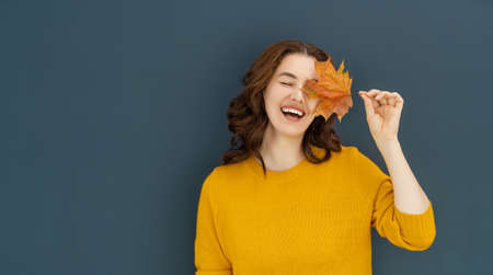 Happy emotional young woman laughing with yellow leaf on dark wall background.の写真素材