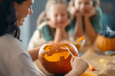 Happy Halloween! Mother and her daughters carving pumpkin. Family preparing for holiday.の写真素材