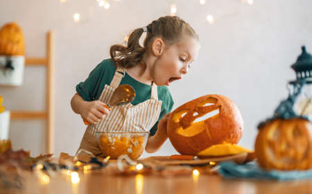 Cute little child girl with carving pumpkin. Happy family preparing for Halloween.の写真素材