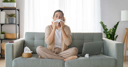 Ill upset girl is holding paper tissue and blowing nose. Virus symptom concept.の写真素材