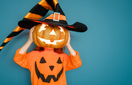 Happy Halloween! Cute little laughing girl in pumpkin costume on blue wall background.の写真素材