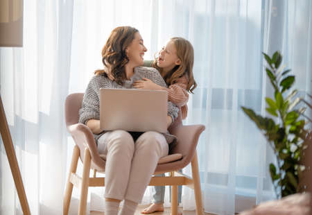 Happy loving family. Young mother and daughter girl using laptop. Funny mom and lovely child are having fun staying at home.の写真素材