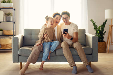 Happy loving family. Young mother, father and daughter using phone. Funny mom, dad and lovely child are having fun staying at home.の写真素材