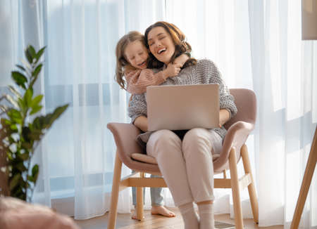 Happy loving family. Young mother and daughter girl using laptop. Funny mom and lovely child are having fun staying at home.の写真素材